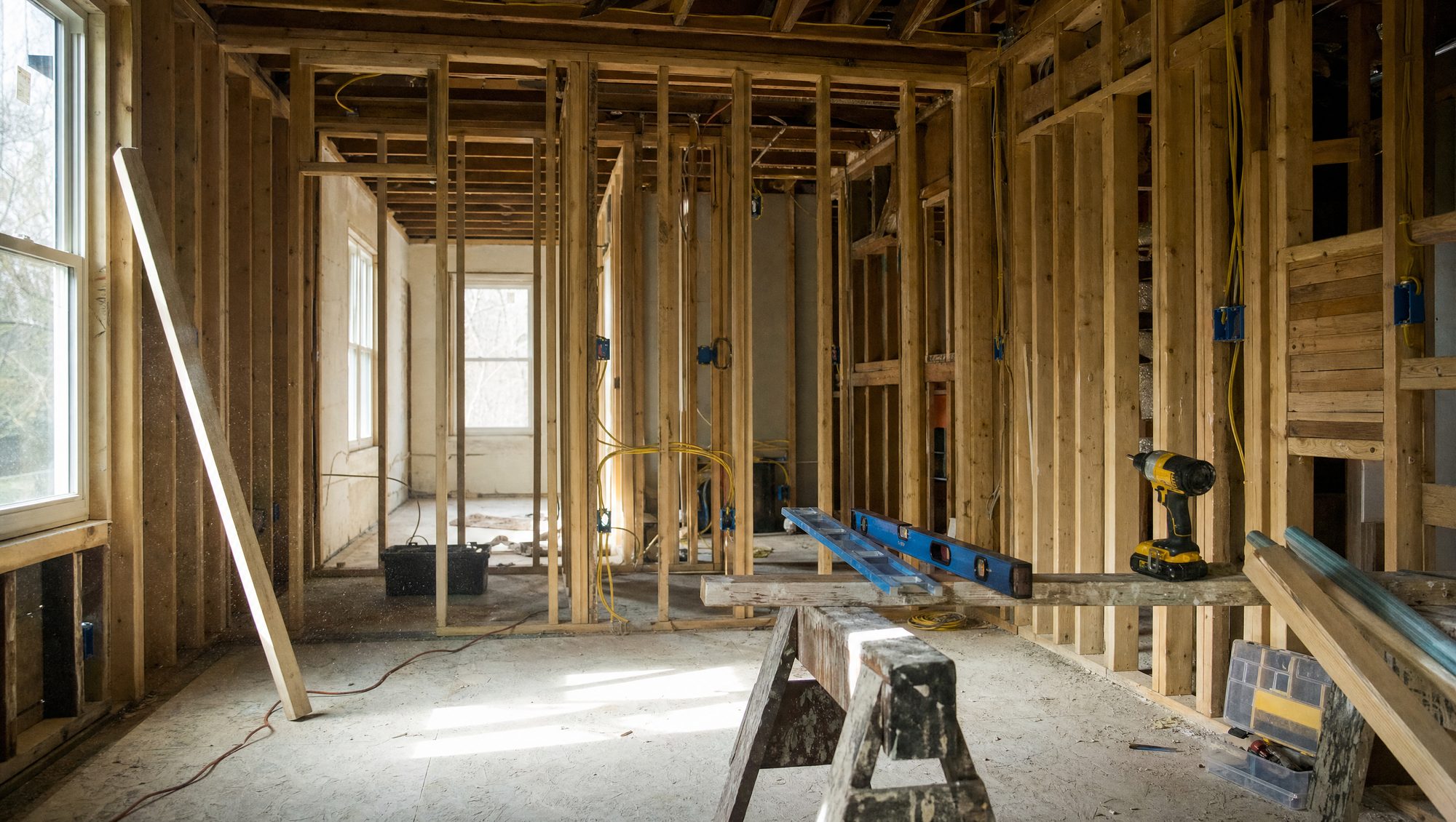Interior of a room stripped to the studs with new electrical wiring and exposed subfloor mid-renovation
